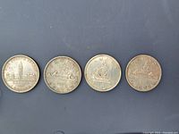 Four loose one-dollar coins: 1939 George VI Jubilee dollar and three Voyageur silver dollars