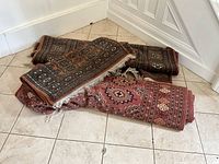 Three rolled oriental rugs stacked on tiled floor