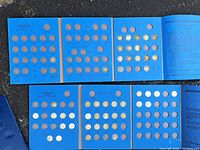 Six blue cardboard coin boards laid out in two rows showing multiple coins inserted in date slots.