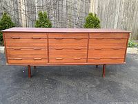 Front view of teak sideboard with nine drawers on paved surface