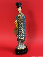 Frontal view of the cloisonné figurine on wood stand against red background