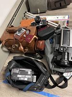 Overall lot showing Sony handycam CCD-TRV40, vintage Balda and Miranda cameras, camera cases, and a tripod on a beige floor.