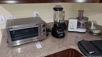 Wide shot showing all three appliances on kitchen counter: toaster oven, blender, and food processor with accessories