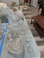Photo of assorted cut glass serving items on table: includes leaf-shaped bowl, covered dishes, cream and sugar set, square box, and small bowls.