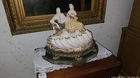 Full view of the figurine lamp showing the couple seated on the shell-shaped porcelain base on metal stand.