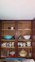 Full cabinet showing contents including turquoise Pyrex bowl, mugs, glassware, and beige tureen