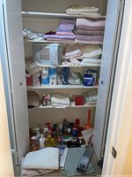 Photo showing closet shelves with stacked towels in pastel colors, folded linens, cleaning sprays, paper products, and health equipment items including a blood pressure monitor and heating pad.