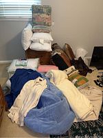 Pillows, blankets, comforter, and robe arranged on a bed and floor showing item details and condition.