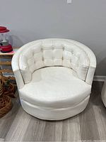 Front view of white vinyl barrel swivel chair with button-tufted back and cushion tear.