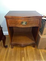 Front view of the wooden nightstand showing drawer with brass handle and open shelf