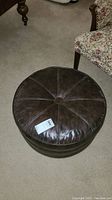 Top view of the vintage round brown leather ottoman with visible stitching and button detail in center.
