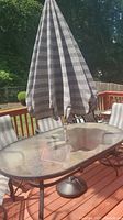 Outdoor deck showing rectangular glass and metal table with closed striped vinyl umbrella in stand.