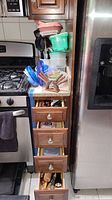 Wide shot showing plastic food containers stacked on countertop, black utensils in holder, drawers slightly open showing cutlery and other kitchen items.