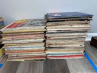 Photo showing two stacks of vinyl record albums placed side by side on the floor, showing the condition and quantity of the lot