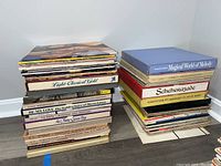 Two stacks of vinyl record albums with visible spines showing various genres including classical, opera, and rock. Albums are stacked vertically.