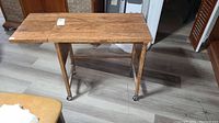 Front view of the vintage wooden rolling cart table with extended drop leaf and caster wheels on the legs.