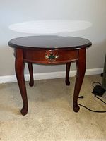 Front view of the round side table showing drawer with brass handle and slipper style legs.
