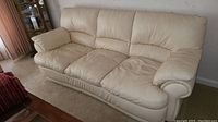 Photo of off white leather sofa showing front and left side with three seat cushions, padded armrests, and segmented back cushions.