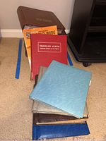Five stamp albums stacked vertically on carpet, one titled 'Traveler Album Postage Stamps of the World' in red cover on top, other four in various brown and blue covers.