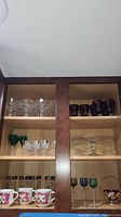 Shelf with multiple glass and crystal stemware including clear, purple, and green glasses and a clear glass cake stand.