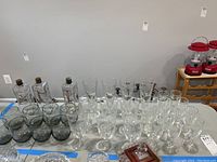 Photo showing wide assortment of clear glass stemware and decanter bottles arranged in rows on a table.