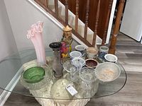 Overview of all glass and ceramic vases, bowls, pots, candle holders and planters arranged on oval glass table.