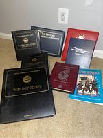 Photo showing seven black, burgundy, red, and blue albums and folders for stamp collections.