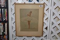 Framed vintage ballerina print hanging on a wall with lattice background, showing full artwork with muted soft colors and signature in corner.