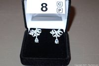 Front view of rhinestone drop earrings placed inside a black velvet jewelry box, showing clear rhinestones with a bow and dangling teardrop design.