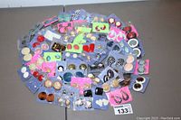Wide shot of 60 pairs of colorful costume jewelry earrings arranged on a table on blue and pink cards