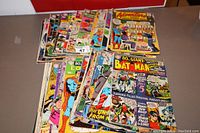 Top view of various Batman and Superman vintage comic books stacked showing different cover arts and titles.