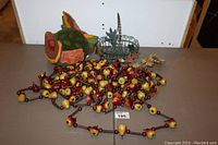 Wide view showing the long garland with small artificial fruits and berry decorations spread on a surface, with green wreath and fabric leaves behind.