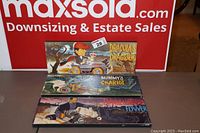 Three vintage promotional signs stacked, showing colorful horror-themed artwork for Dracula's Dragster, Mummy's Chariot, and Frankenstein's Flivver, with a maxsold.com backdrop.