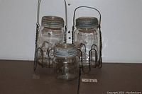 Five vintage mason jars including two large jars with metal lids in wire carriers and one smaller jar in front.