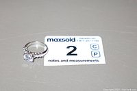 Clear silver-tone ladies ring with large clear center gemstone and smaller side stones on band, photographed on gray surface