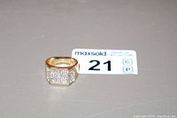 Front and angled view of men's gold tone ring encrusted with small clear stones in rectangular shape on top.