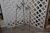 Full view of metal picture easel showing the overall shape and design against a lattice background.