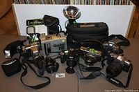 Full lot view showing multiple cameras, flash units, camera bags and accessories on table.