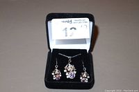 Photo of necklace pendant and matching earrings inside a black jewelry box showing the cluster of purple and clear stones.