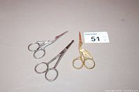 Photo showing three sewing scissors including one gold-toned with stork design and two silver-toned with heron designs on handles, placed on a light surface with maxsold lot tag visible.