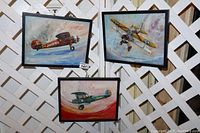 Three vintage airplane paintings hanging on white lattice backdrop, showing all three artworks in one view