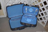 Open view of two vintage suitcases showing blue quilted satin interiors with elastic and fabric compartments.