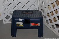 Blue Rubbermaid tool box bench stool with visible latch and handle, photographed from front and above angles showing textured top and signs of use and dirt.