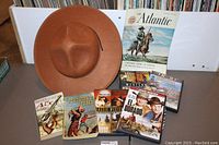 Western-themed accessories lot with Mountie-style hat, DVDs, and magazines displayed on a wooden table.