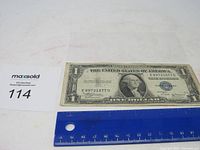 Front side photo of the 1935 B Blue Seal Silver Certificate $1 bill, placed alongside a blue ruler for scale.