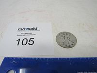 1935 D Standing Liberty half dollar coin placed beside a ruler and MaxSold lot card number 105.