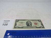 Photo of the 1953 $2 bill front side placed on ruler showing size, with MaxSold lot number visible.