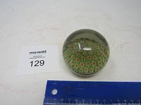 Glass paperweight with green millefiori floral pattern and scale ruler for size reference.