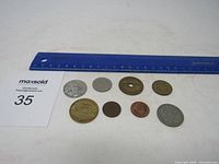 Top-down view of the 7 coins next to a blue ruler and a Maxsold lot card showing the lot number 35.