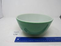 Front view of green Pyrex bowl showing size with ruler for scale.